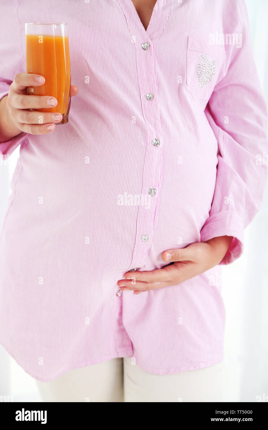 Young pregnant woman holding glass of juice on light background Stock ...