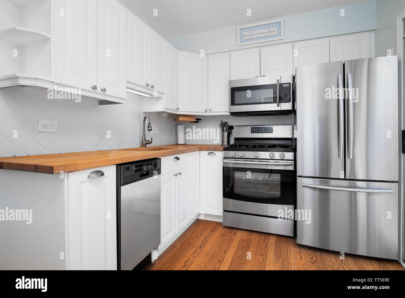 A small kitchen with stainless steel appliances, white cabinets, and a natural light colored wood counter top. Stock Photo