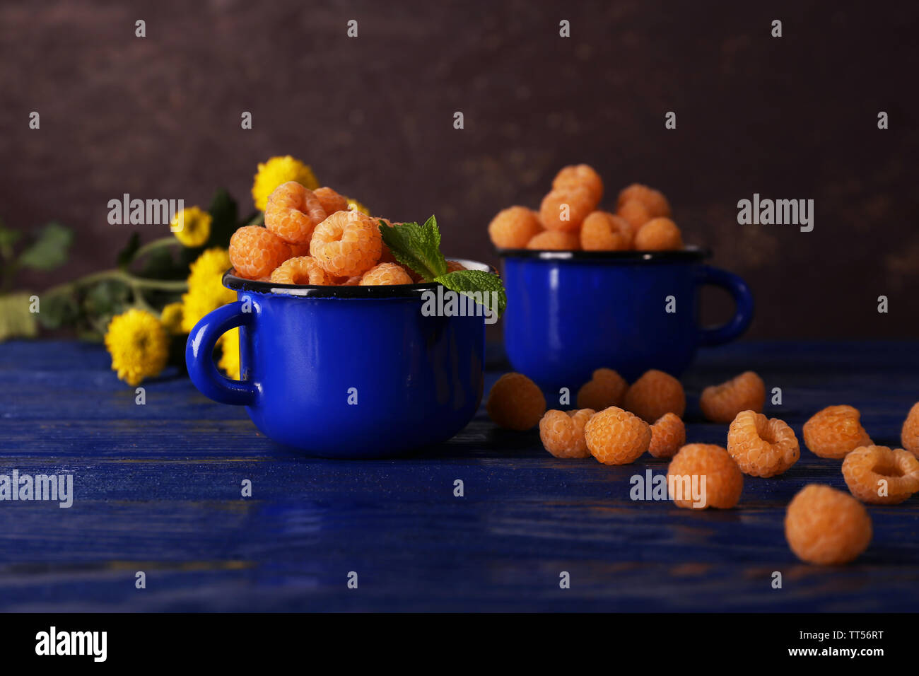 Yellow raspberries in dark blue mugs and wildflowers on wooden table on