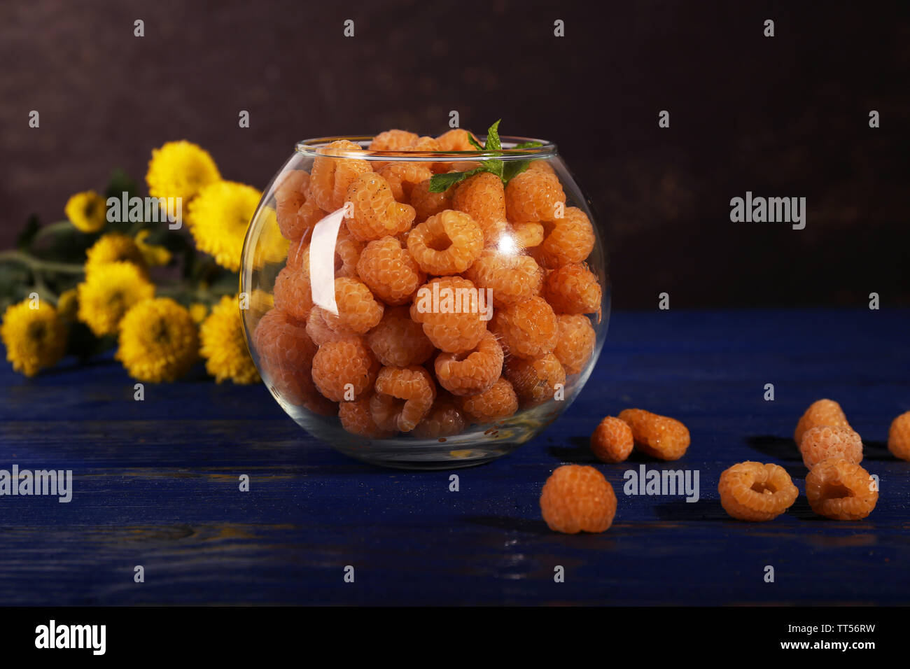 Raspberries in glass and wildflowers on dark blue wooden table on dark