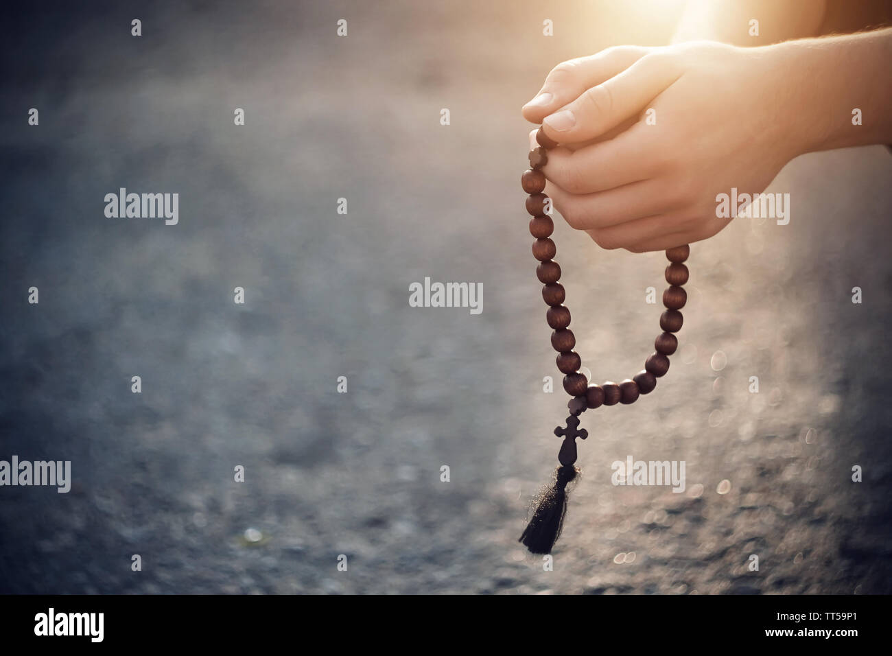 The Christian holds in his hands, folded in prayer, wooden rosaries, on which the light of heavenly illumination falls. Stock Photo