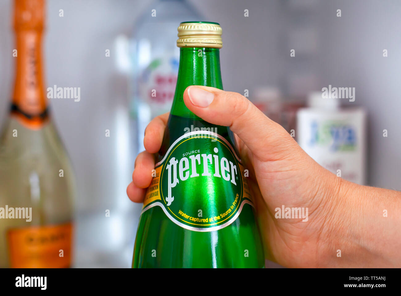 Tambov, Russian Federation - June 10, 2019 Close-up of woman hand taking out bottle with Perrier water from fridge. Stock Photo