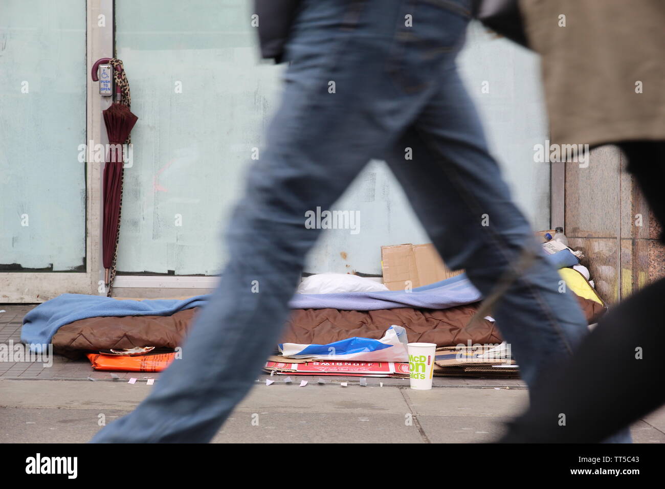 People walking past a homeless spot at the entrance of a closed down ...