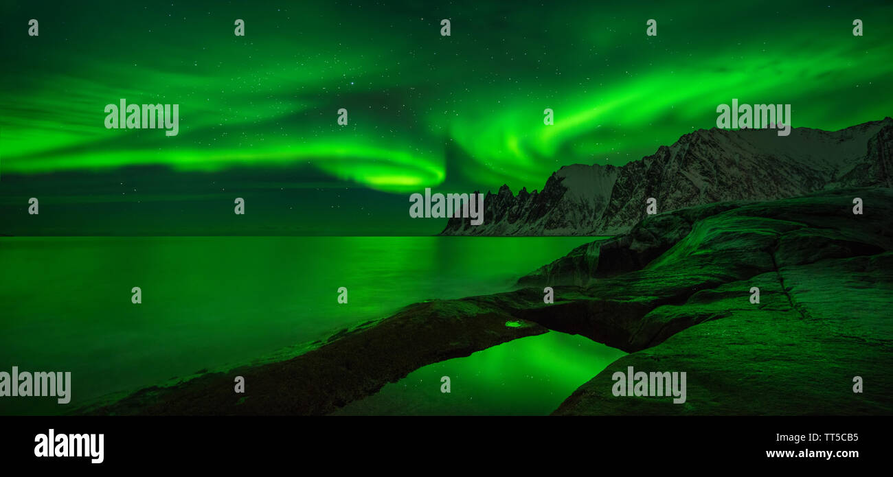 Panorama of aurora over Tugeneset rocky coast with mountains in background, Senja, Norway Stock Photo
