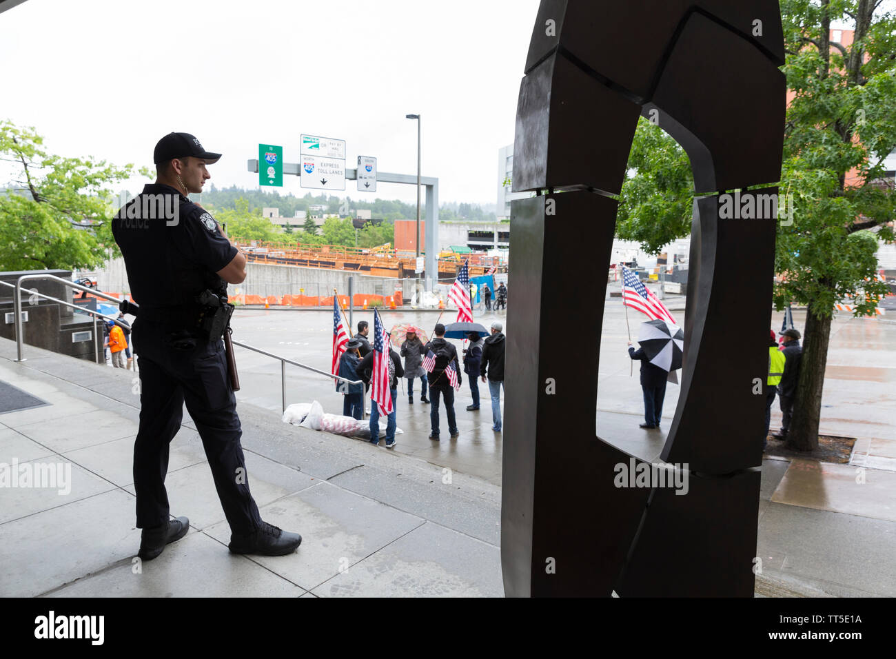 A member of the Bellevue Police watches as protesters gather against Rep. Ilhan Omar in Bellevue, Washington on Saturday, May 25, 2019. Patriots of Washington lead the protest against the representative who was headlining a CAIR-WA Ramadan fundraiser. Stock Photo