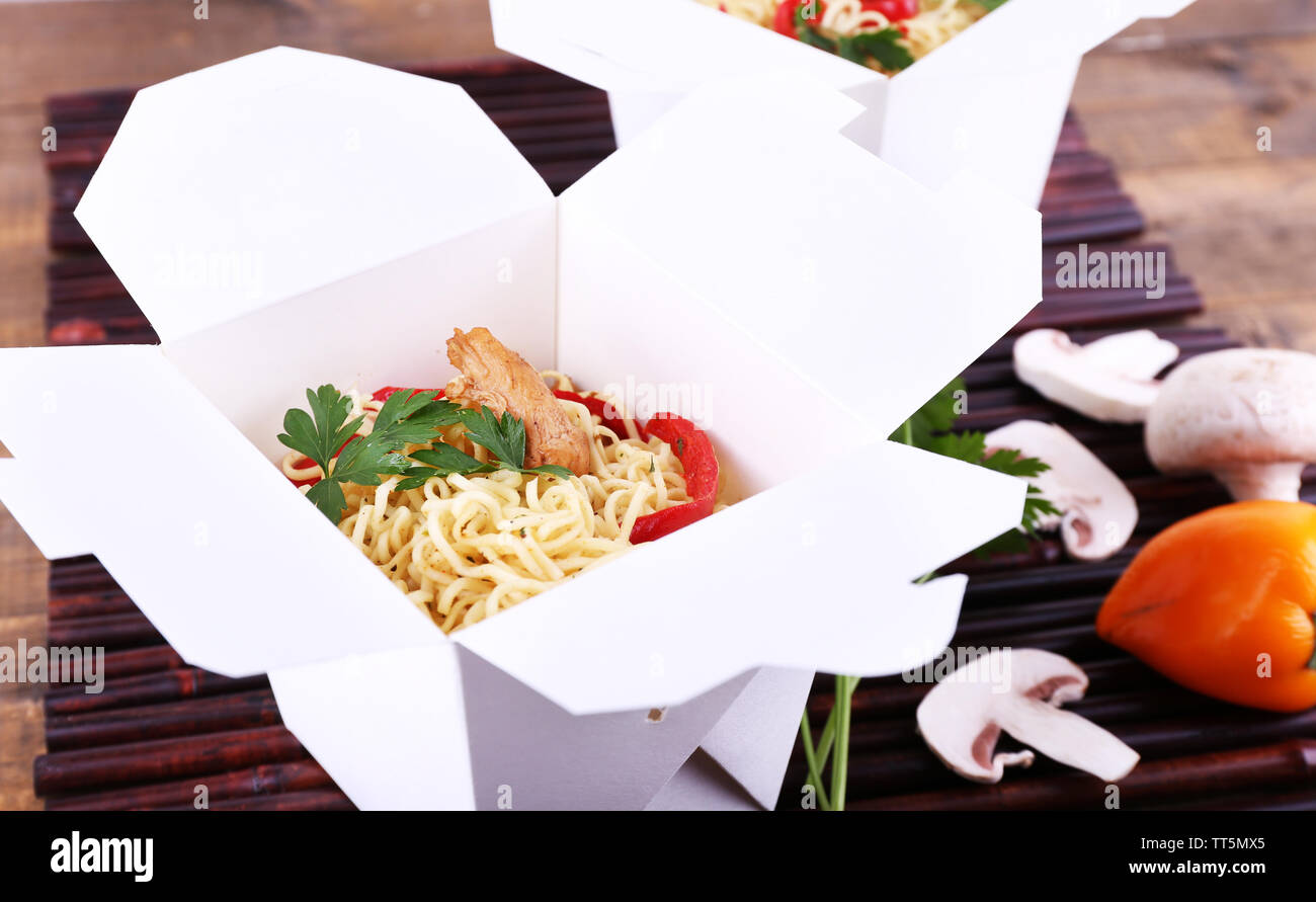 Chinese noodles in takeaway boxes on bamboo mat background Stock Photo