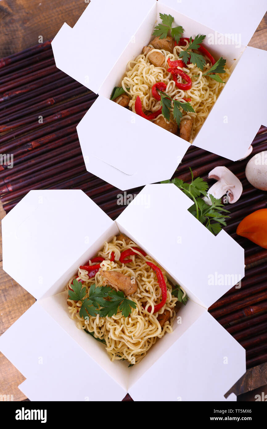 Chinese noodles in takeaway boxes on bamboo mat background Stock Photo