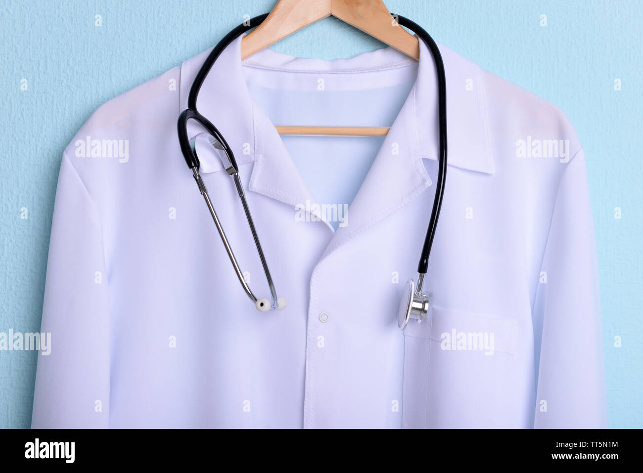 Doctor coat with stethoscope on hanger on blue background Stock Photo