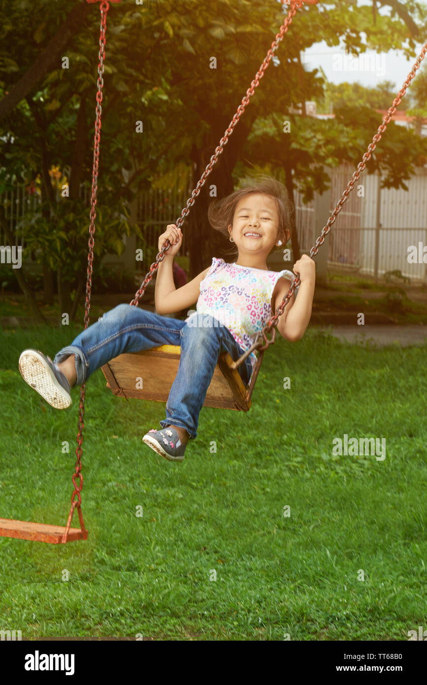 Asian kid in playground hang on swings in sunny bright day background Stock Photo