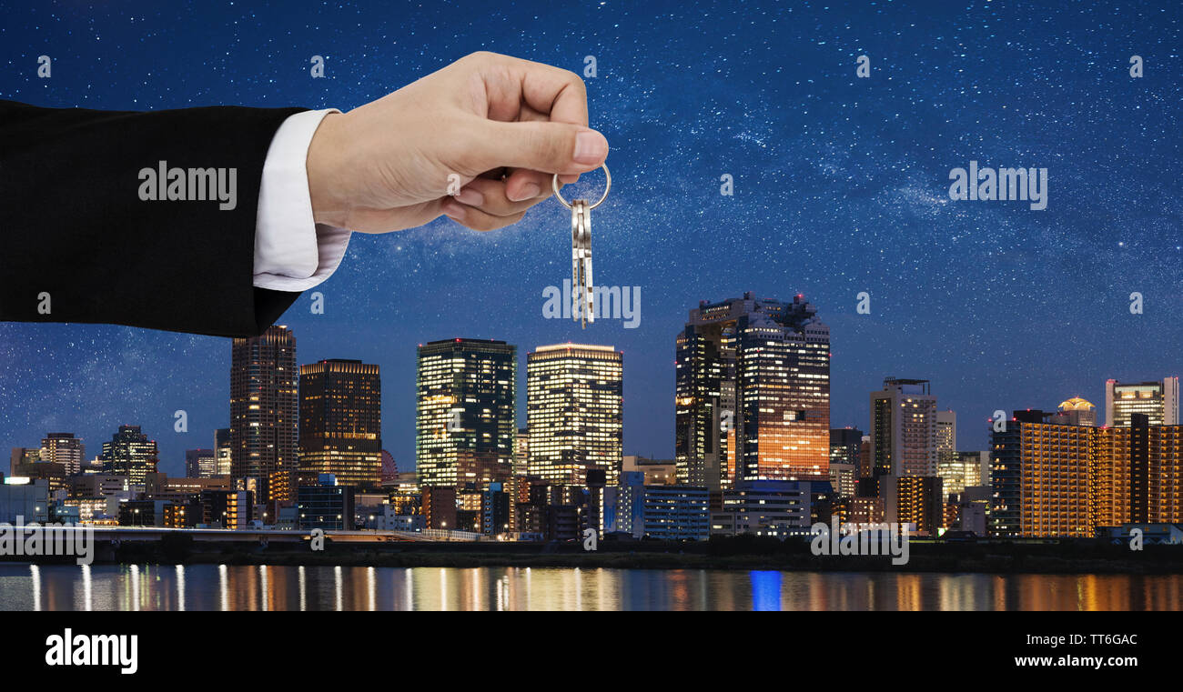 Real estate business, residential rental and investment. Businessman handover keys, with city at night background Stock Photo