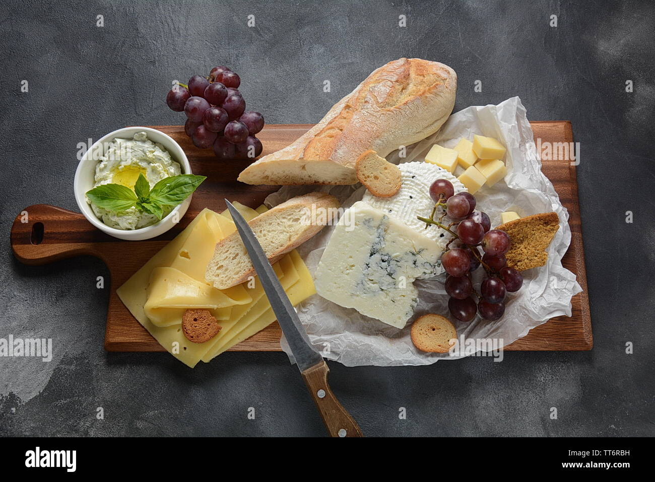 Cheese platter with assorted cheese, grapes, snacks on dark background