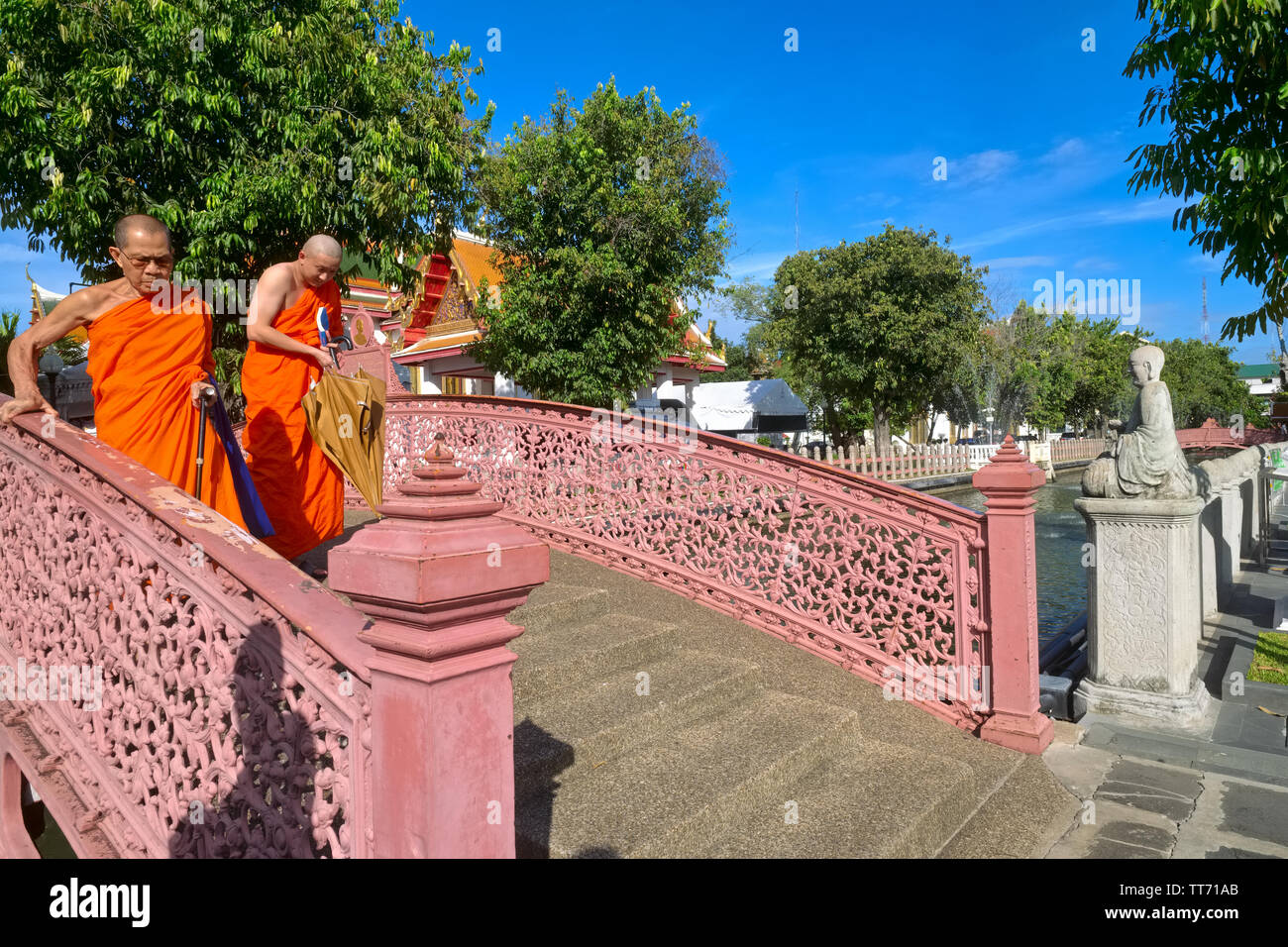 Two senior Buddhist monks passing a sloped klong (canal) bridge in the idyllic grounds of Wat