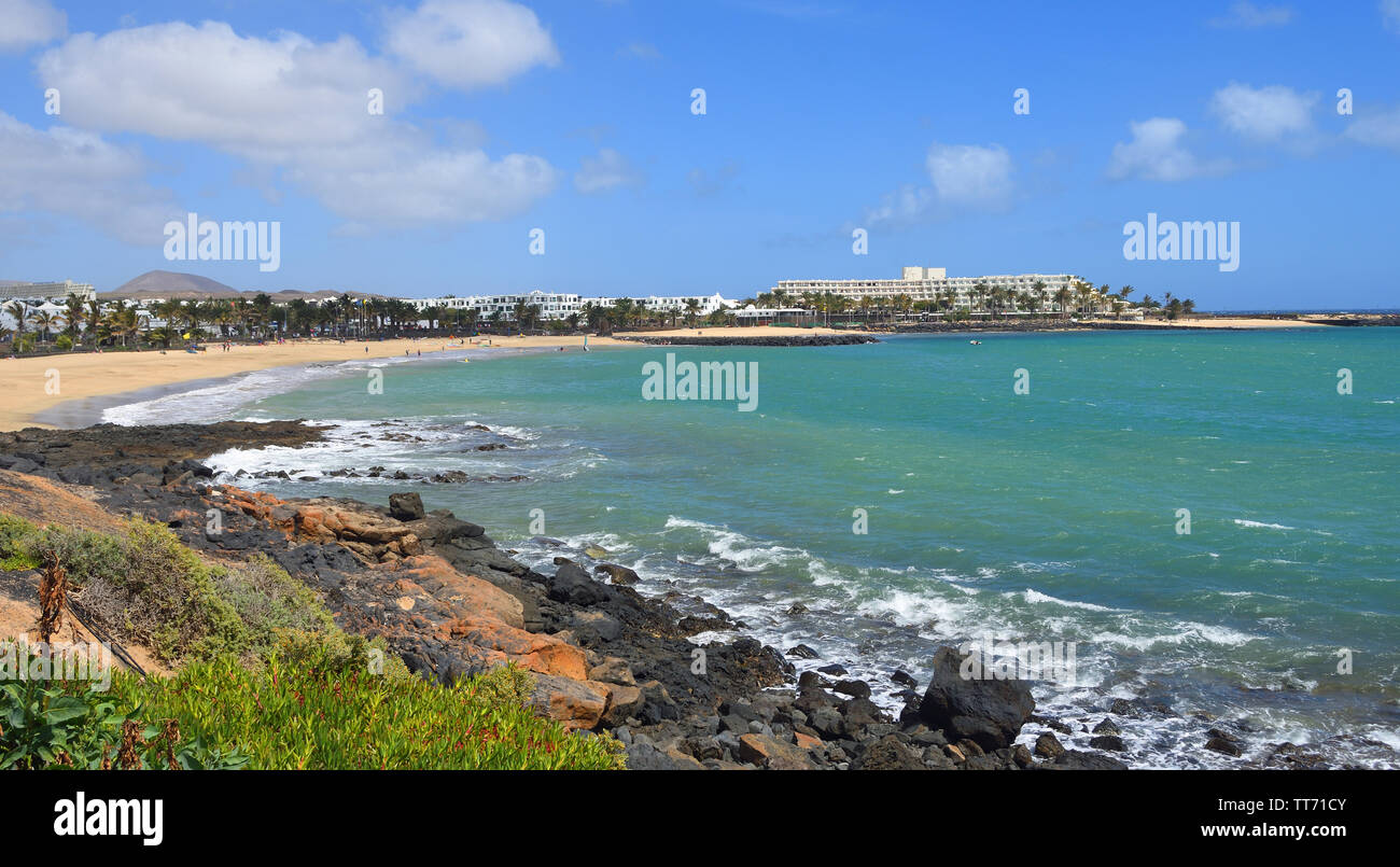 View of the Beach at Costa Teguise Lanzarote  with Orange Flowers in the Forground. Stock Photo