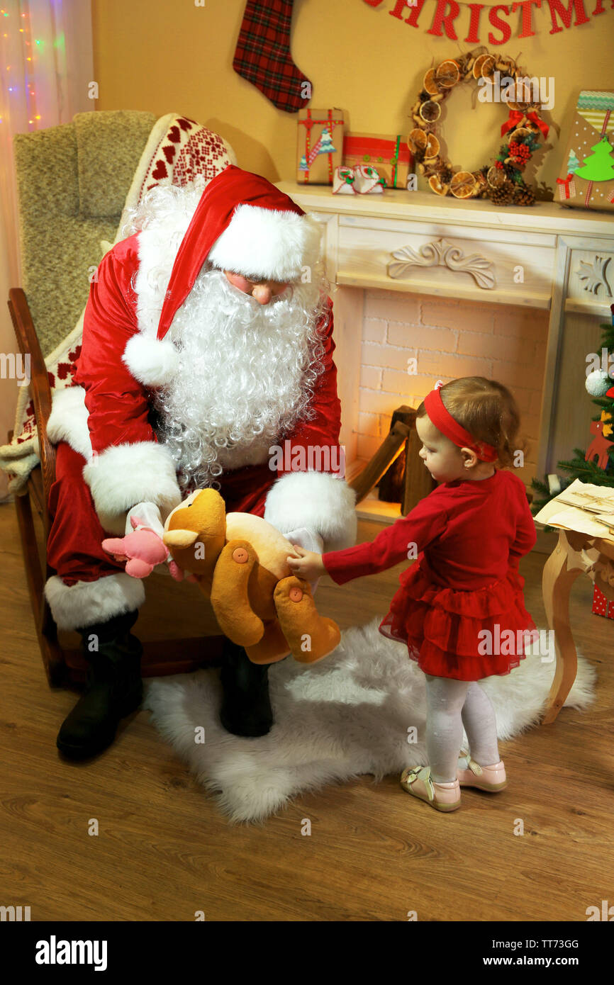 Santa Claus giving present to little cute girl near fireplace and ...
