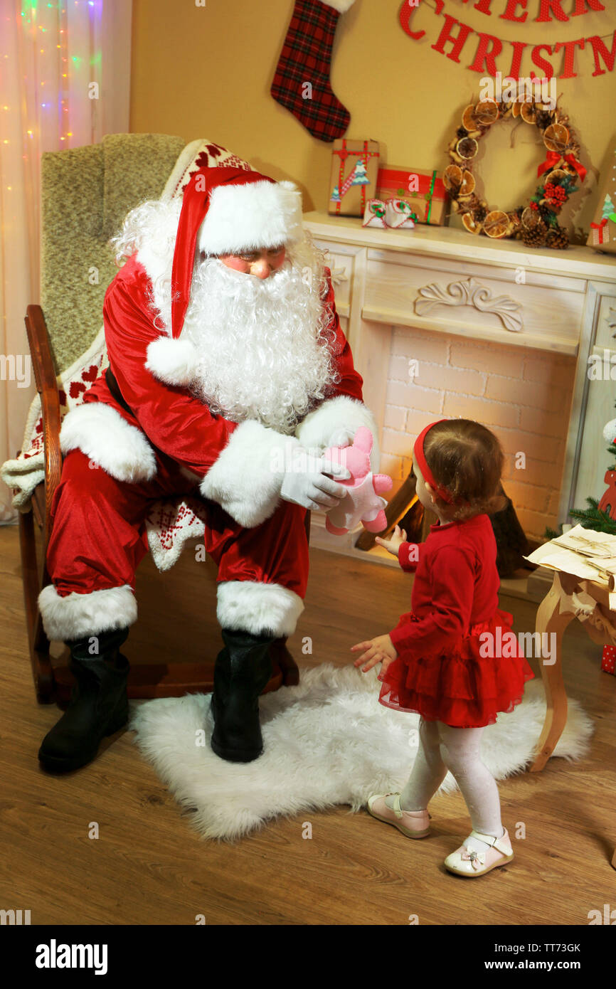 Santa Claus giving present to little cute girl near fireplace and ...