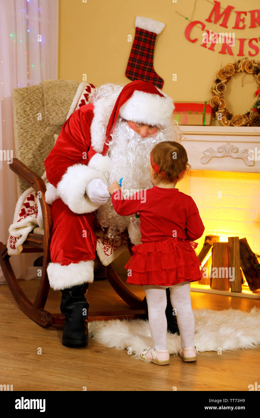 Santa Claus giving present to little cute girl near fireplace and ...