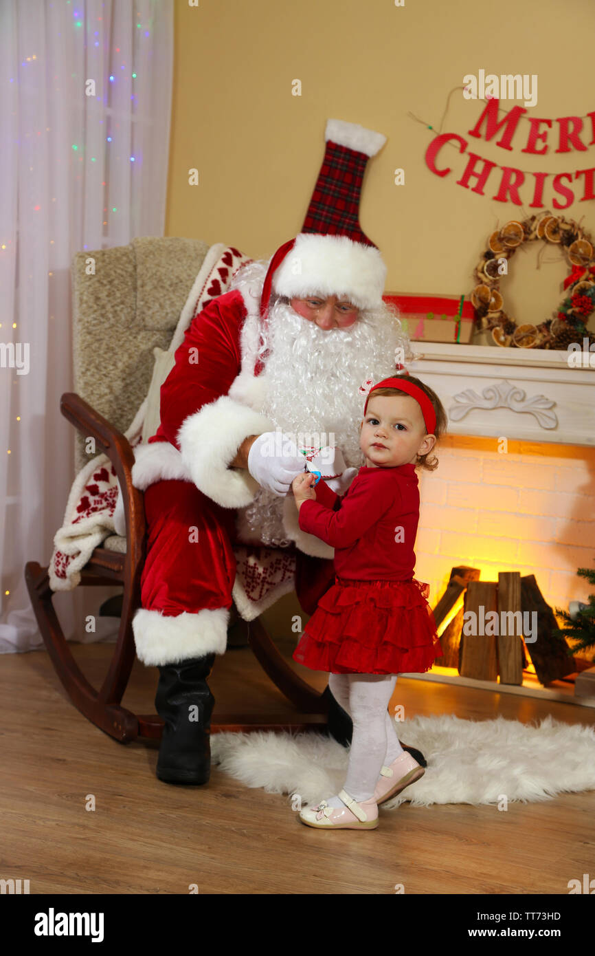 Santa Claus giving present to little cute girl near fireplace and ...