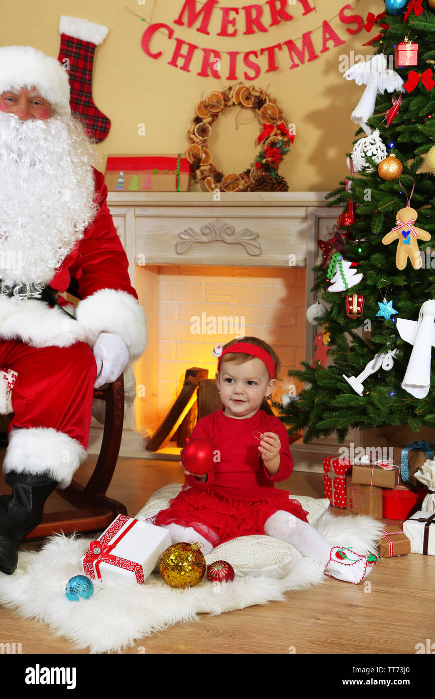 Santa Claus giving present to little cute girl near fireplace and ...
