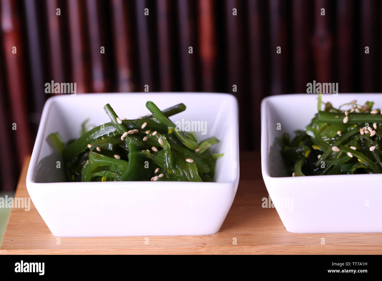 Seaweed salad with cherry tomatoes on wooden stand and bamboo on background Stock Photo