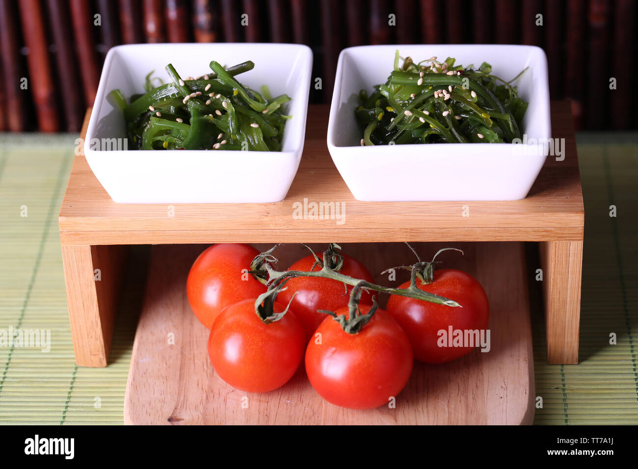 Seaweed salad with cherry tomatoes on wooden stand and bamboo on background Stock Photo