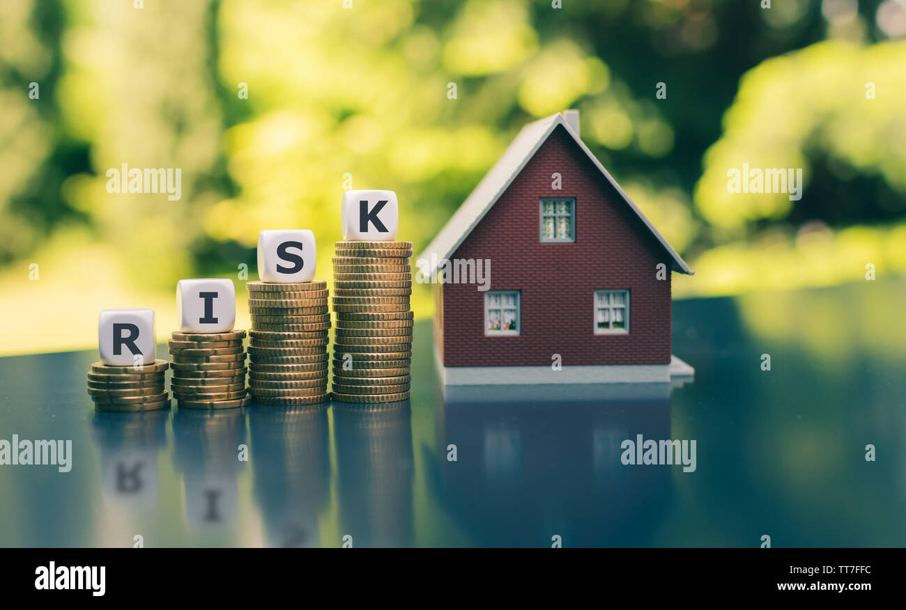 Concept of the financial risk to buy a house. Dice form the word 'risk' placed on increasing high stacks of coins next to a model house. Stock Photo