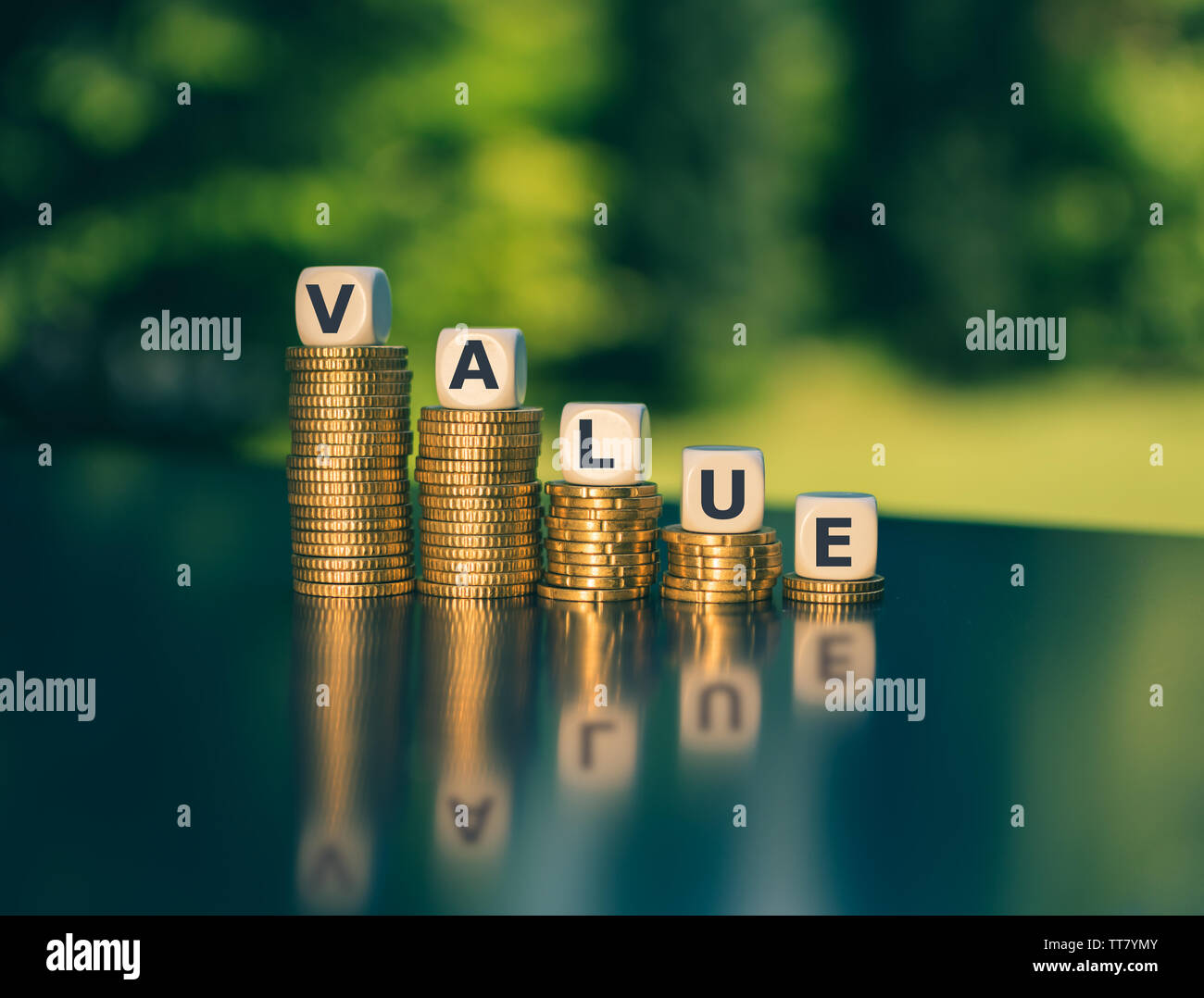Symbol for decreasing value. Dice form the word 'value' on decreasing stacks of coins. Stock Photo