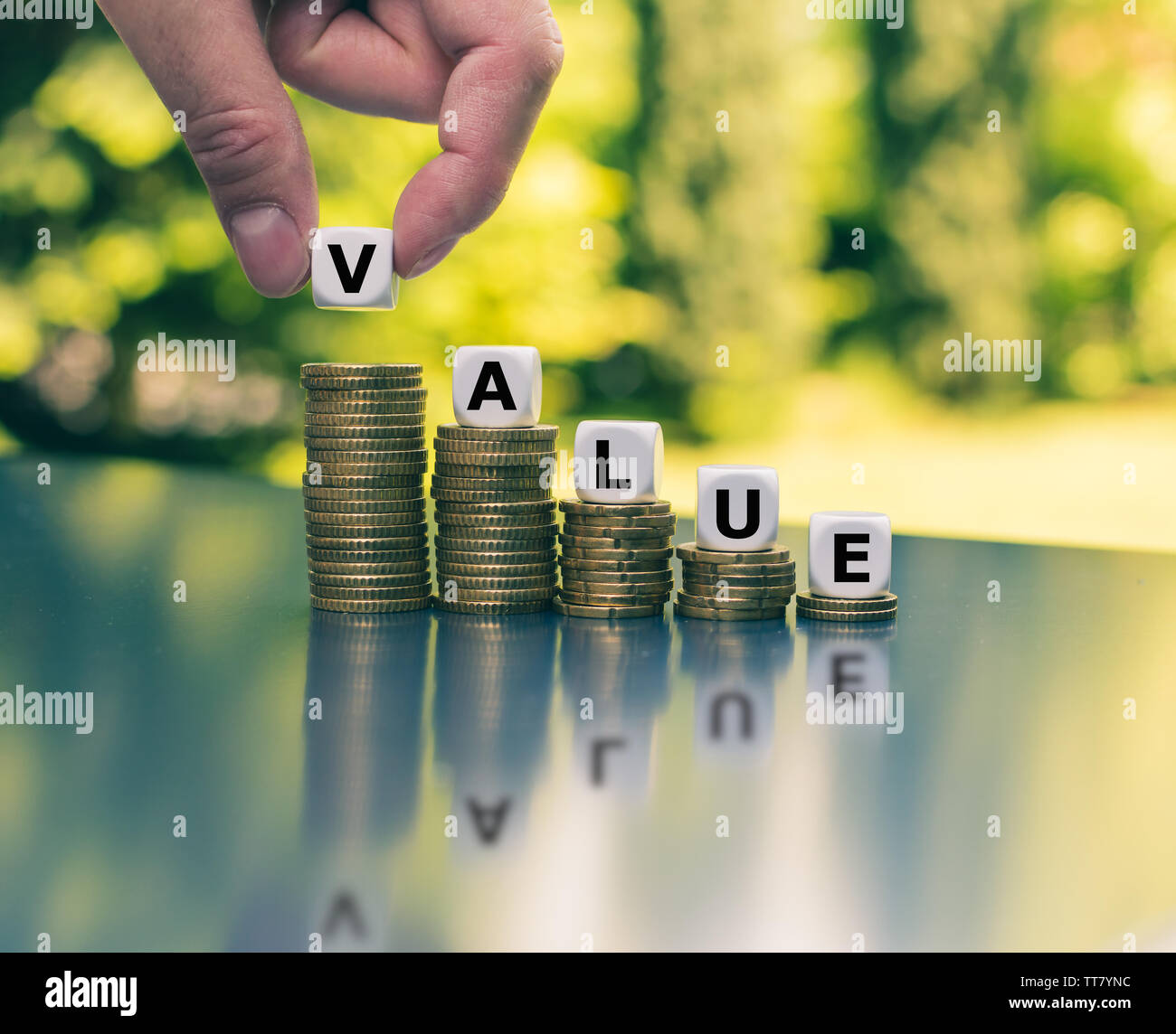 Symbol for decreasing value. Dice form the word 'value' on decreasing stacks of coins. Stock Photo