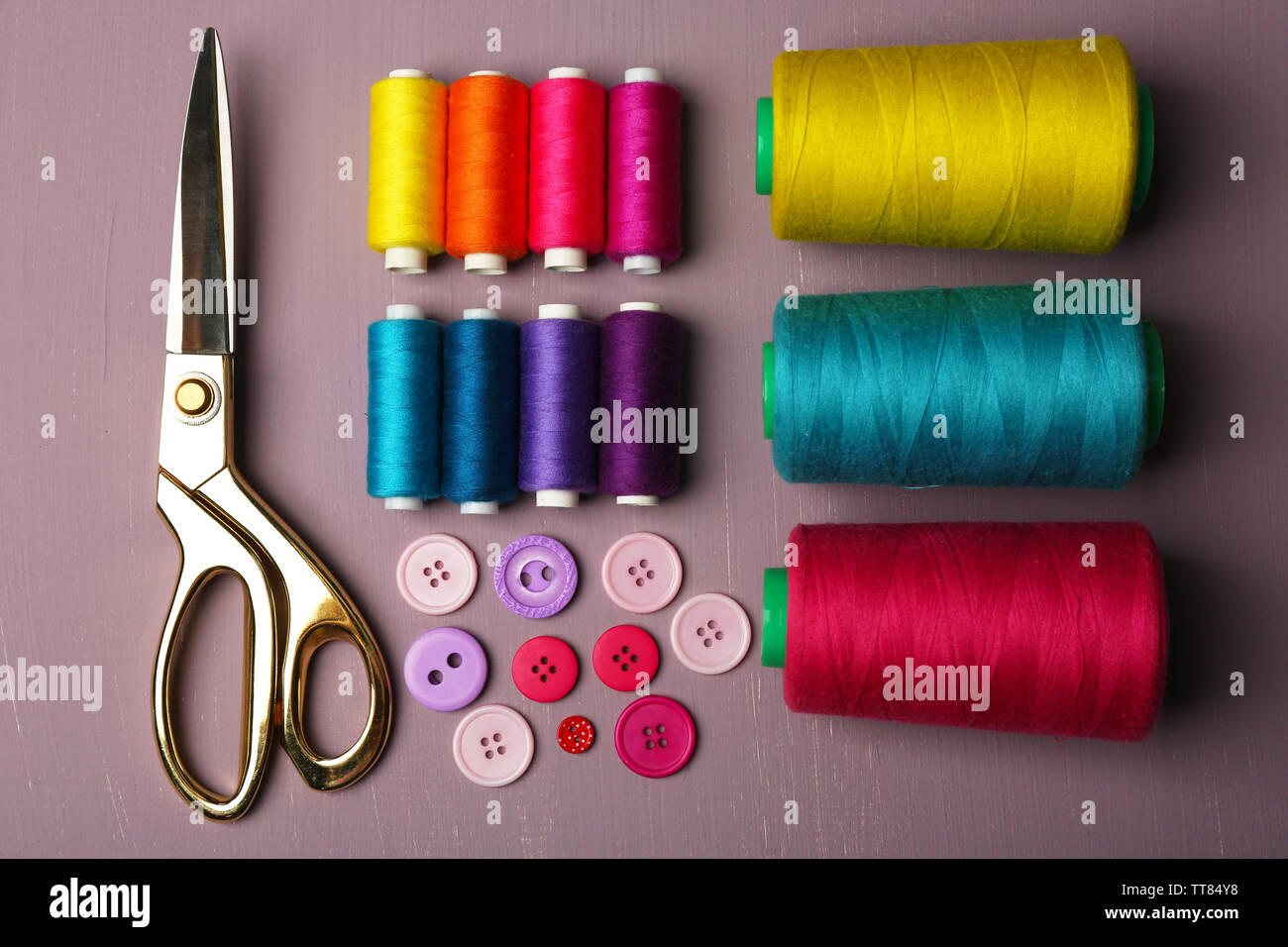 Multicolor sewing threads with buttons and scissors on wooden background Stock Photo
