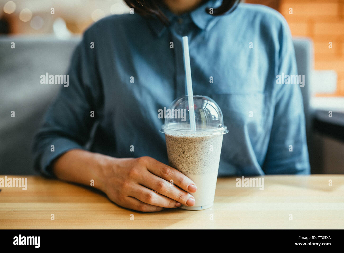 https://c8.alamy.com/comp/TT85XA/girl-in-a-blue-shirt-is-holding-a-plastic-cup-with-milkshake-sitting-in-a-restaurant-TT85XA.jpg