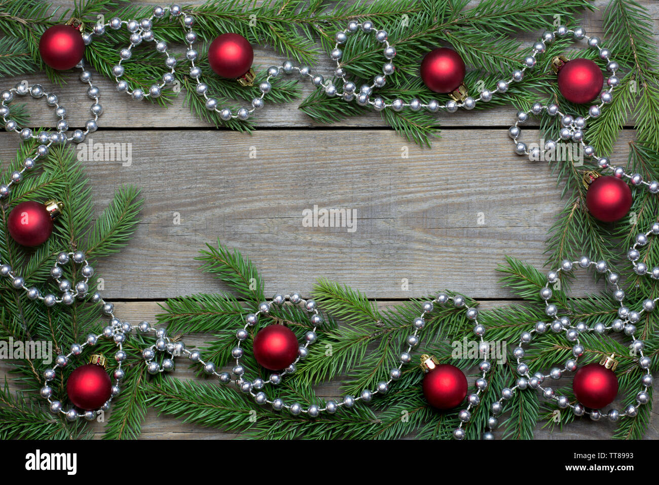 Christmas card concept with fir tree branches, red baubles and silver bead chain on wooden background - text space Stock Photo