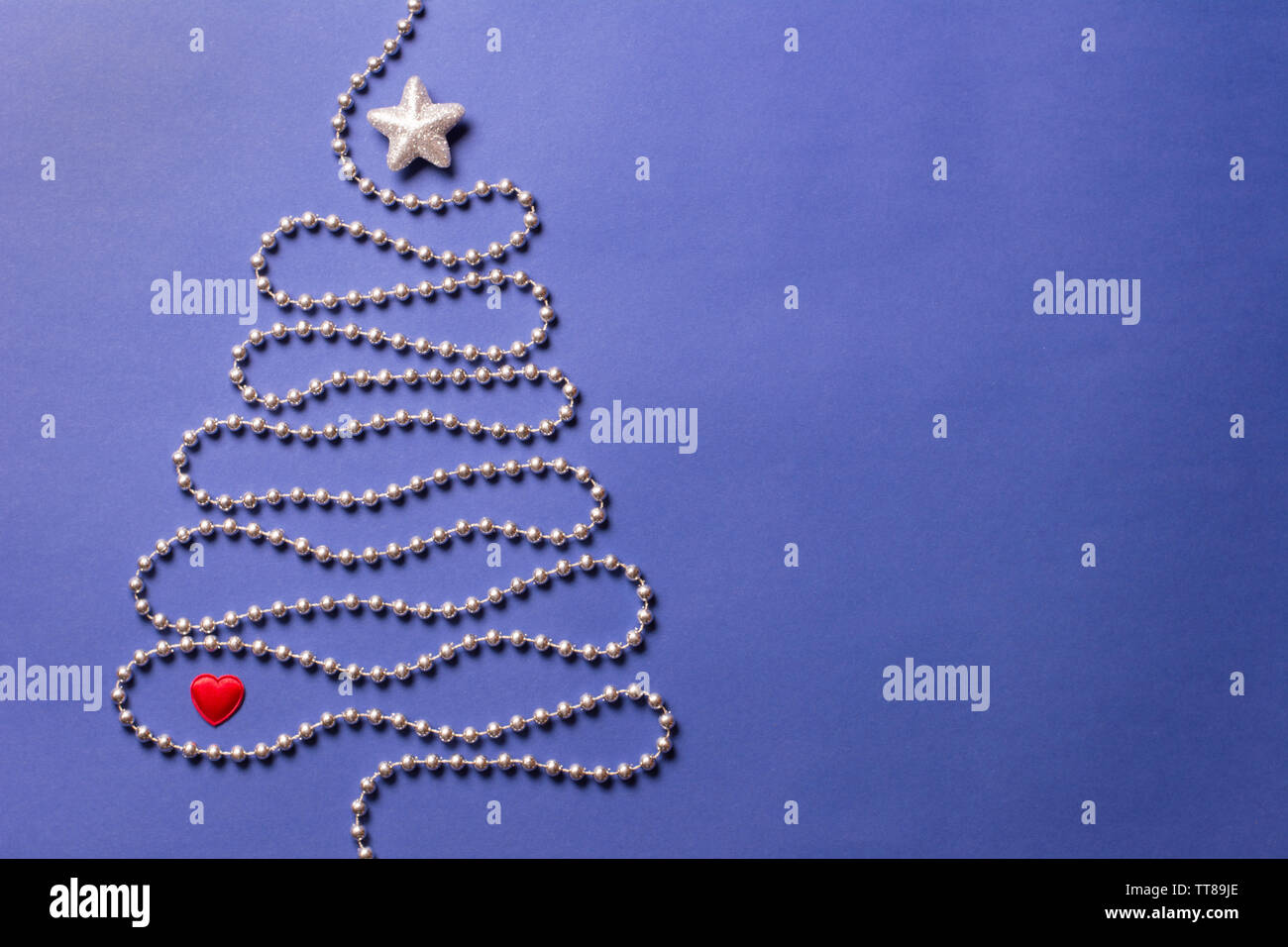 Simple christmas tree concept with silver bead chain, brocade star and red heart on dark blue background - text space Stock Photo