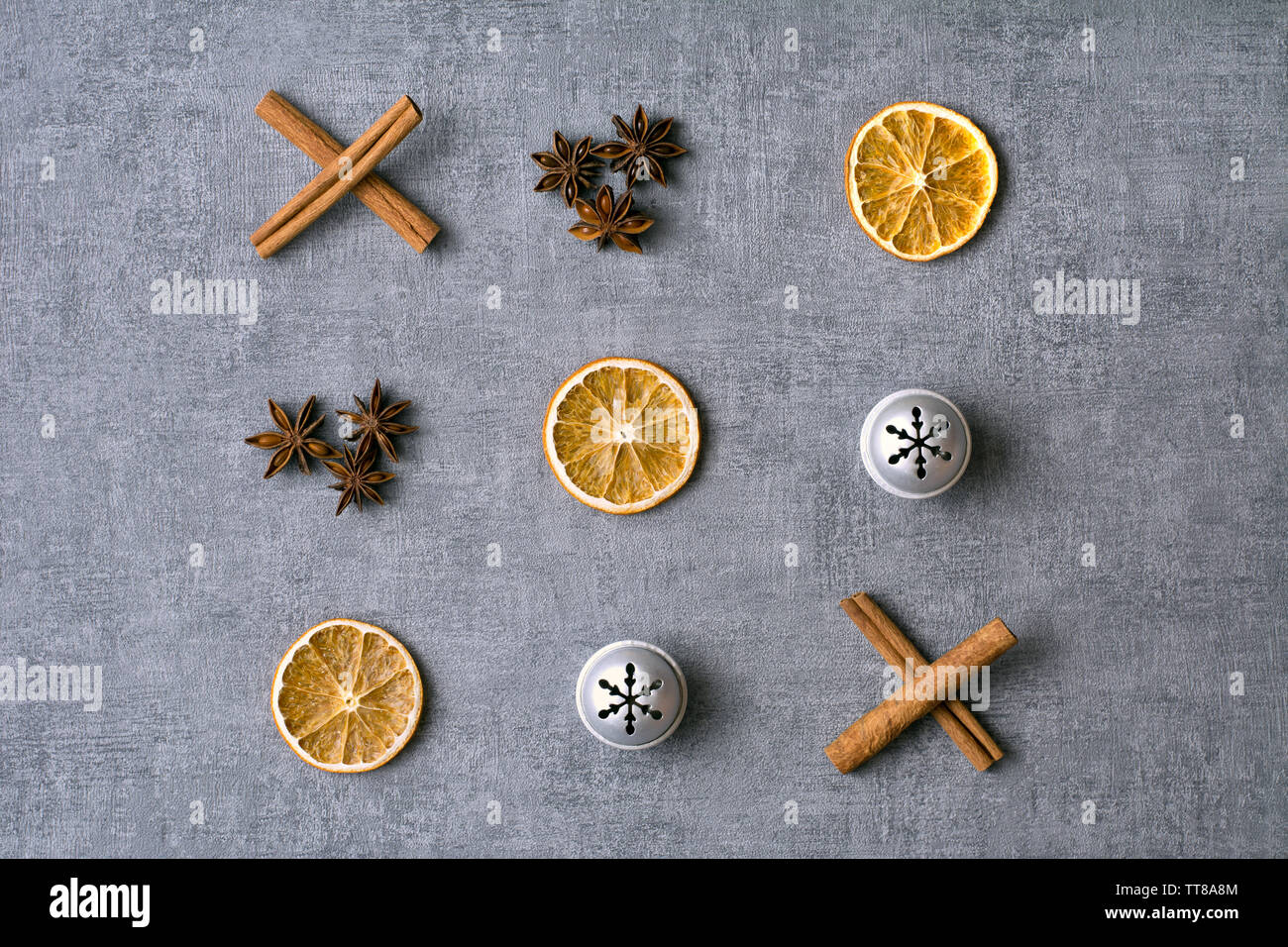 Christmas noughts and crosses deco with dried oranges, aniseeds, cinamon sticks and silver bells on grey background Stock Photo