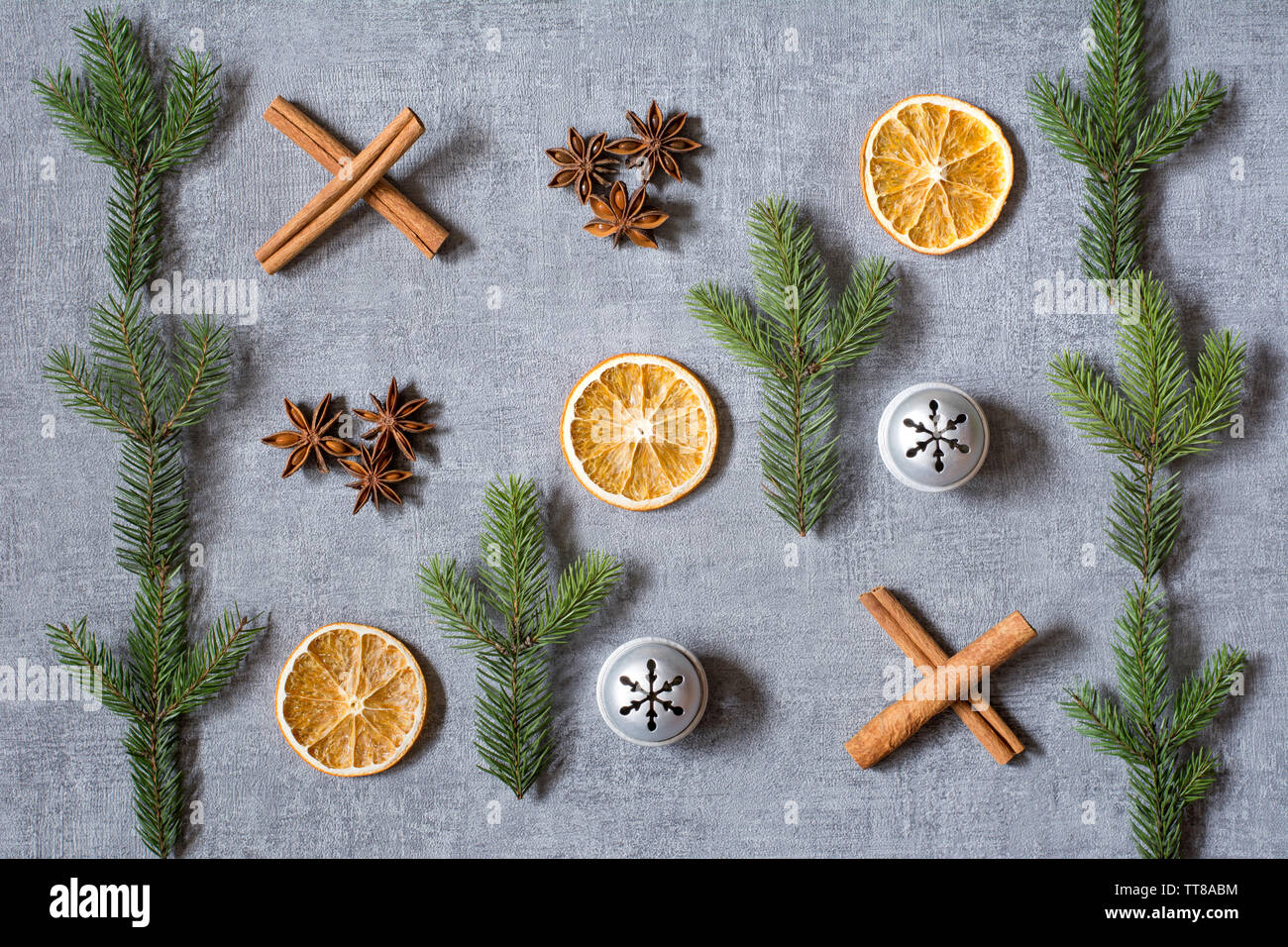 Christmas noughts and crosses deco with dried oranges, aniseeds, cinamon sticks, fir tree branches and silver bells on grey background Stock Photo