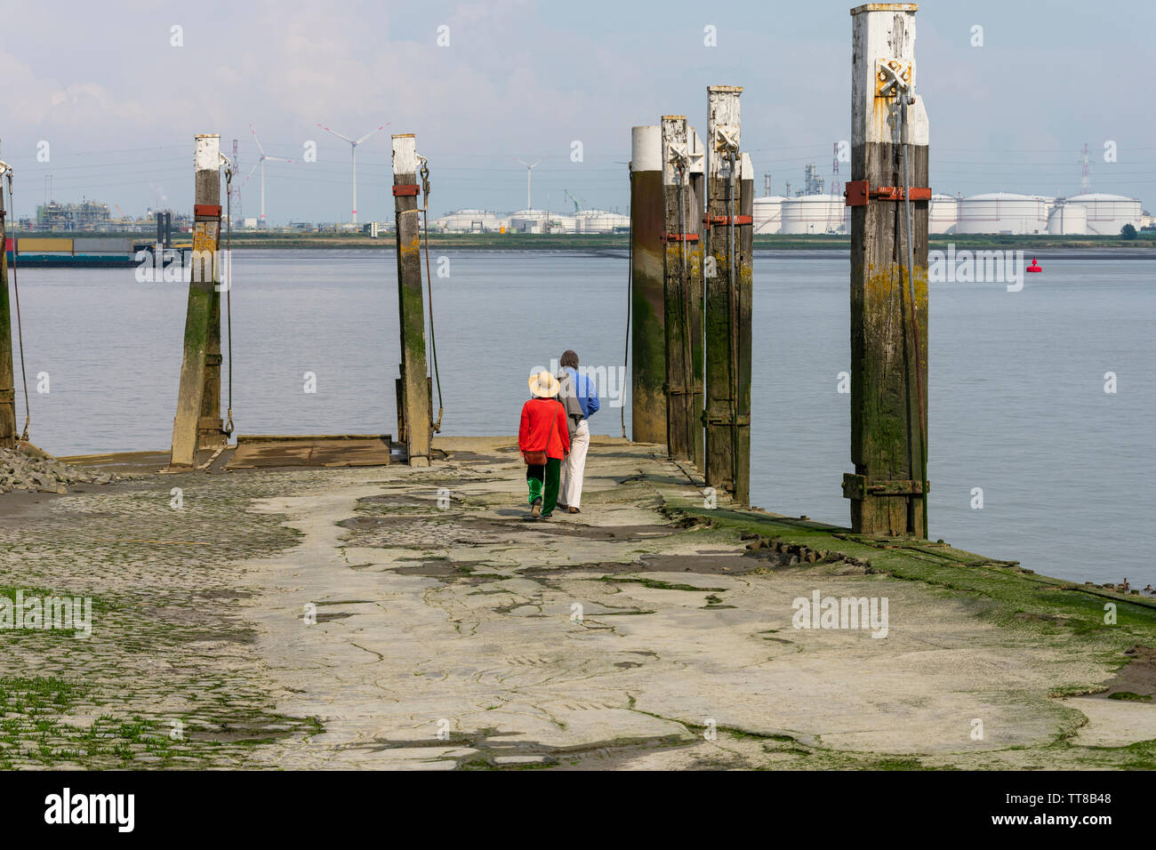 Older couple walks on the quay to the water to watch the ships sail and enjoy the Western Scheldt in Antwerp Belgium Stock Photo