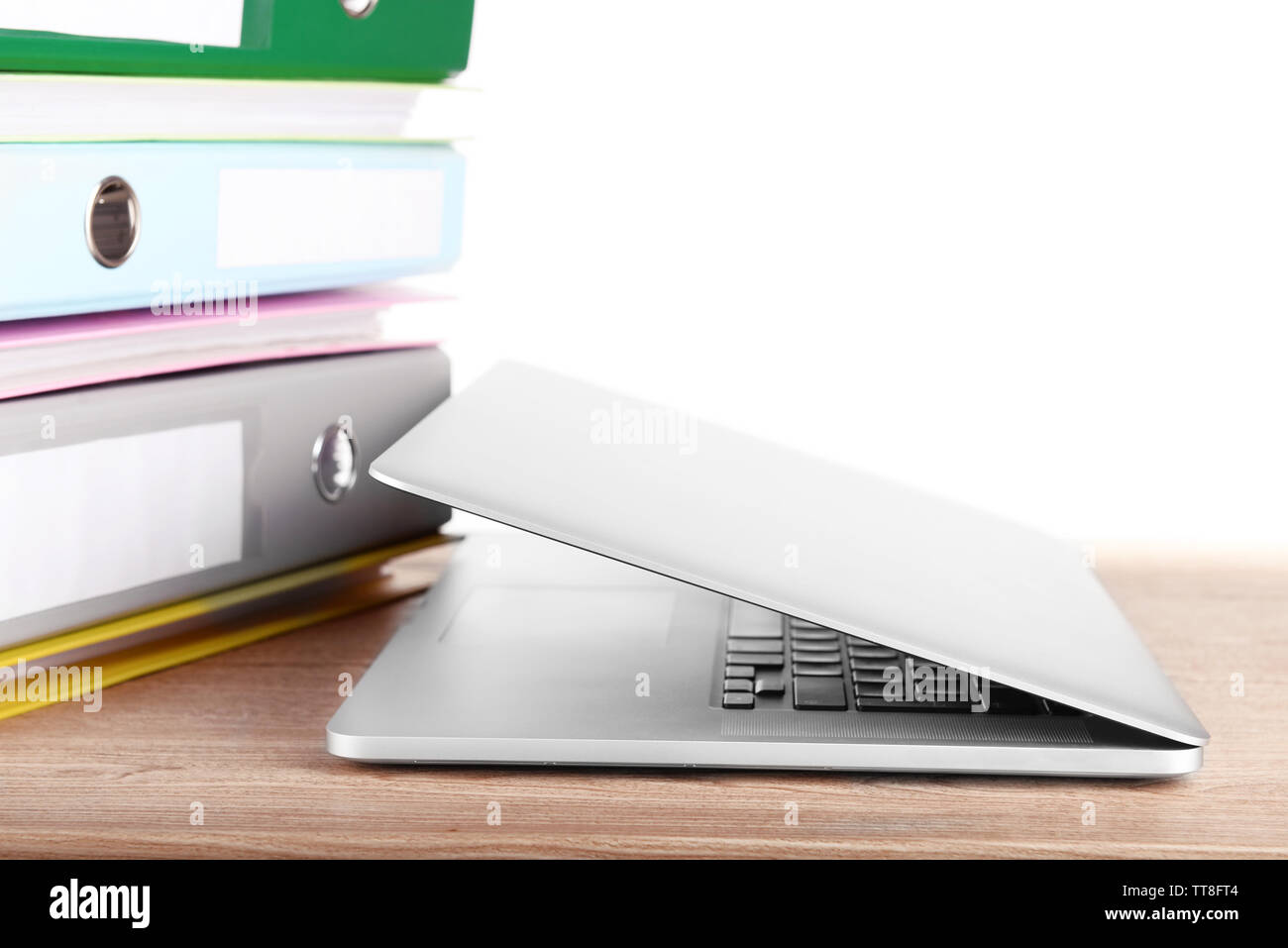 Laptop with stack of folders on table on white background Stock Photo