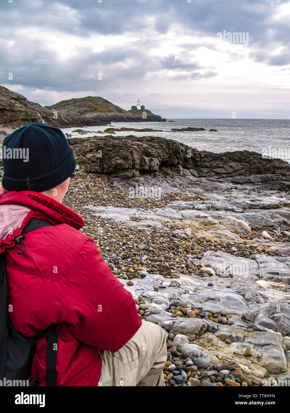 A hiker sits and admires the view from Bracelet Bay beach. The Mumbles lighthouse on Mumbles Head can be seen from here. Swansea, Gower, Wales, UK. Stock Photo