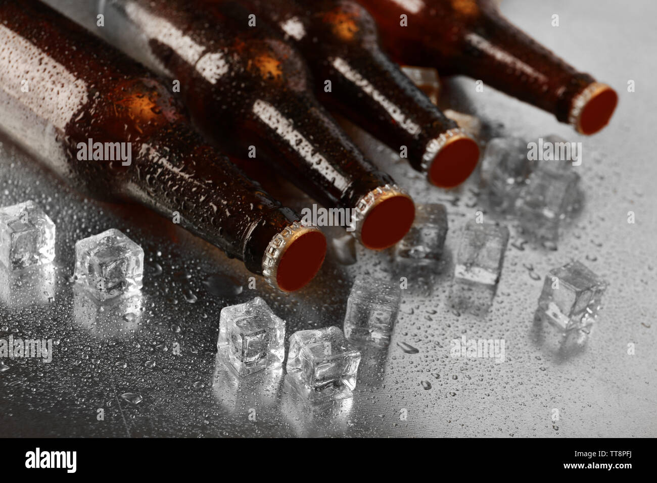Glass bottles of beer with ice cubes on wet table background Stock