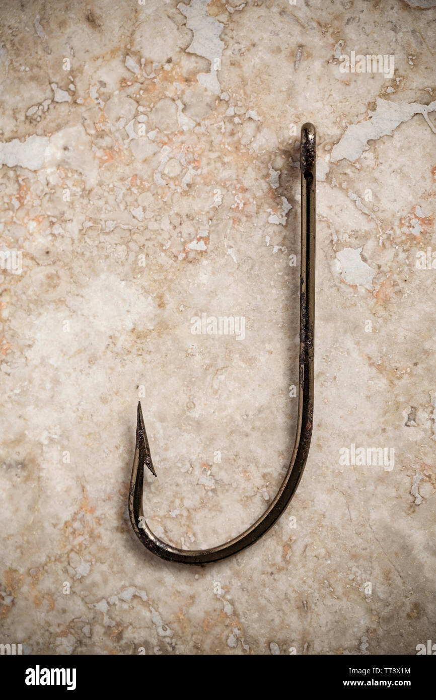 A single large seafishing hook displayed on a stone background. Hooks are equipped with barbs to stop them falling out of a hooked fish and to prevent Stock Photo