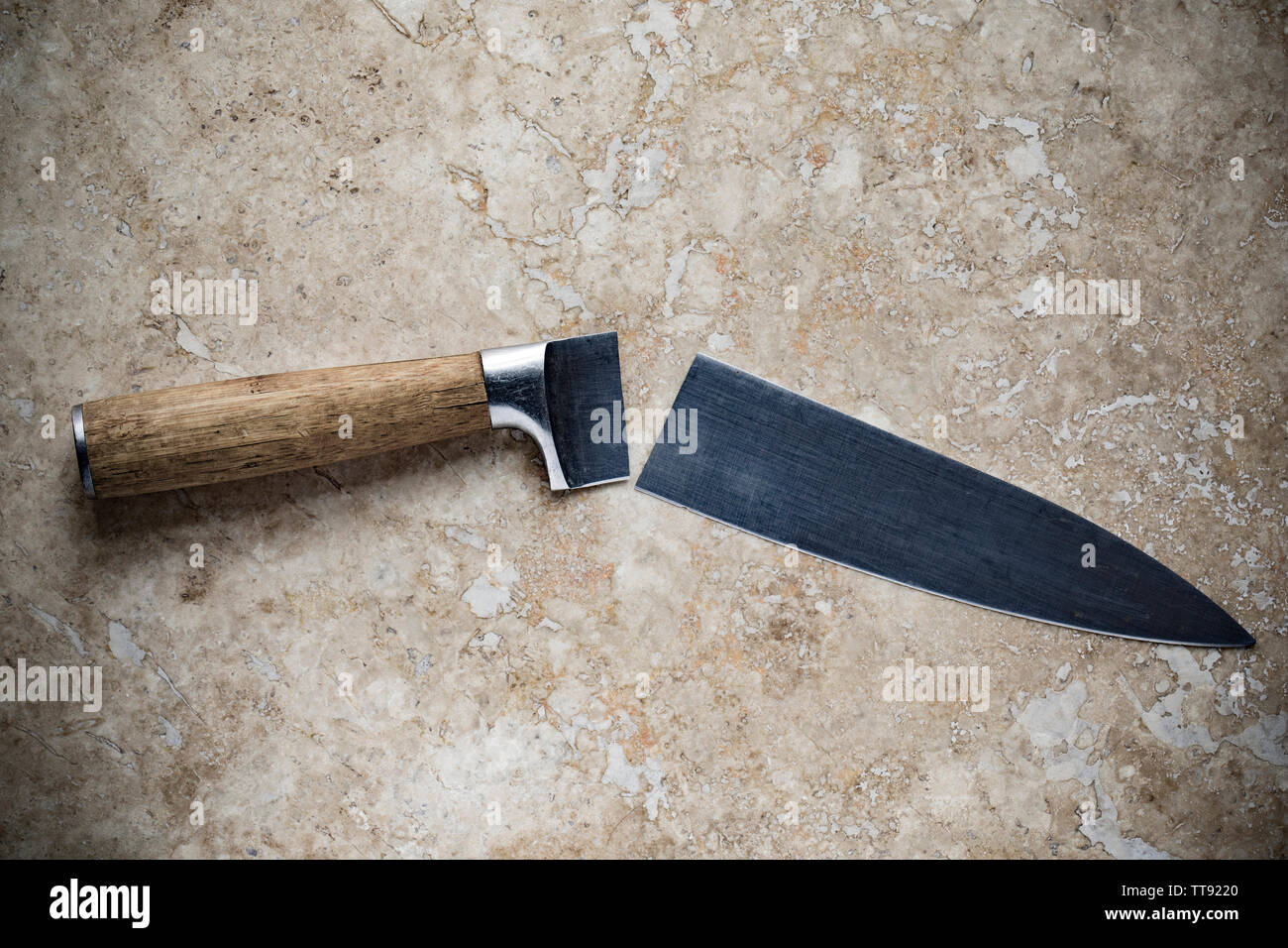 A broken kitchen knife displayed on a light stone background