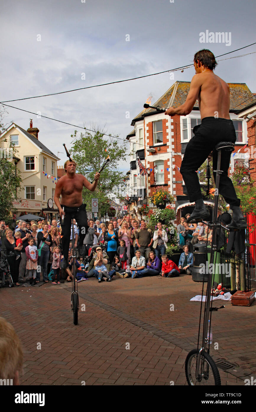 SIDMOUTH, DEVON, ENGLAND - AUGUST 5TH 2012: Two street jugglers and entertainers perform with unicycles and fire clubs in the town square to an apprec Stock Photo