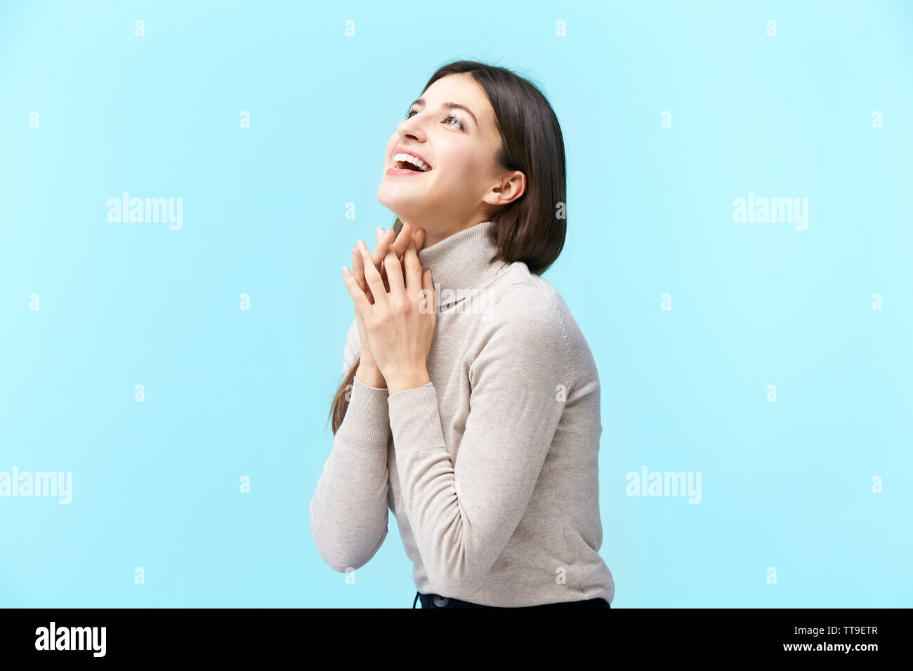 happy and smiling young caucasian woman looking up at the sky, isolated on blue background. Stock Photo