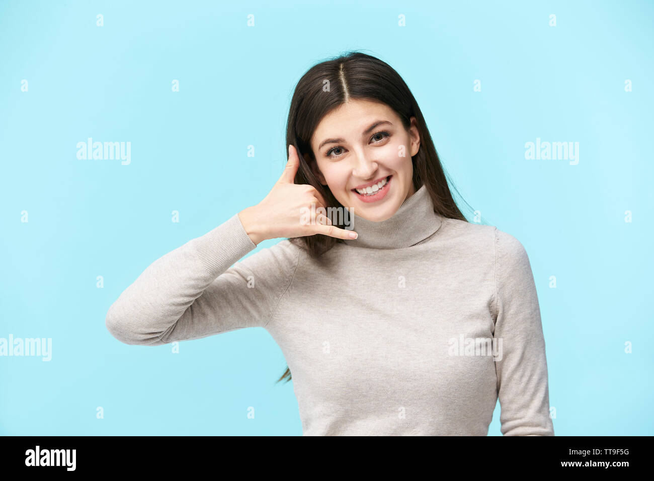 beautiful young caucasian woman making a call me hand sign, looking at camera smiling, isolated on blue background Stock Photo