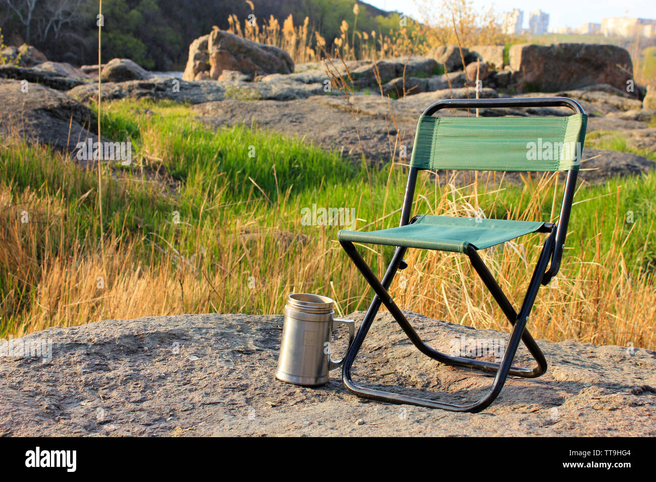 Camp chair and thermos cup on nature background Stock Photo -