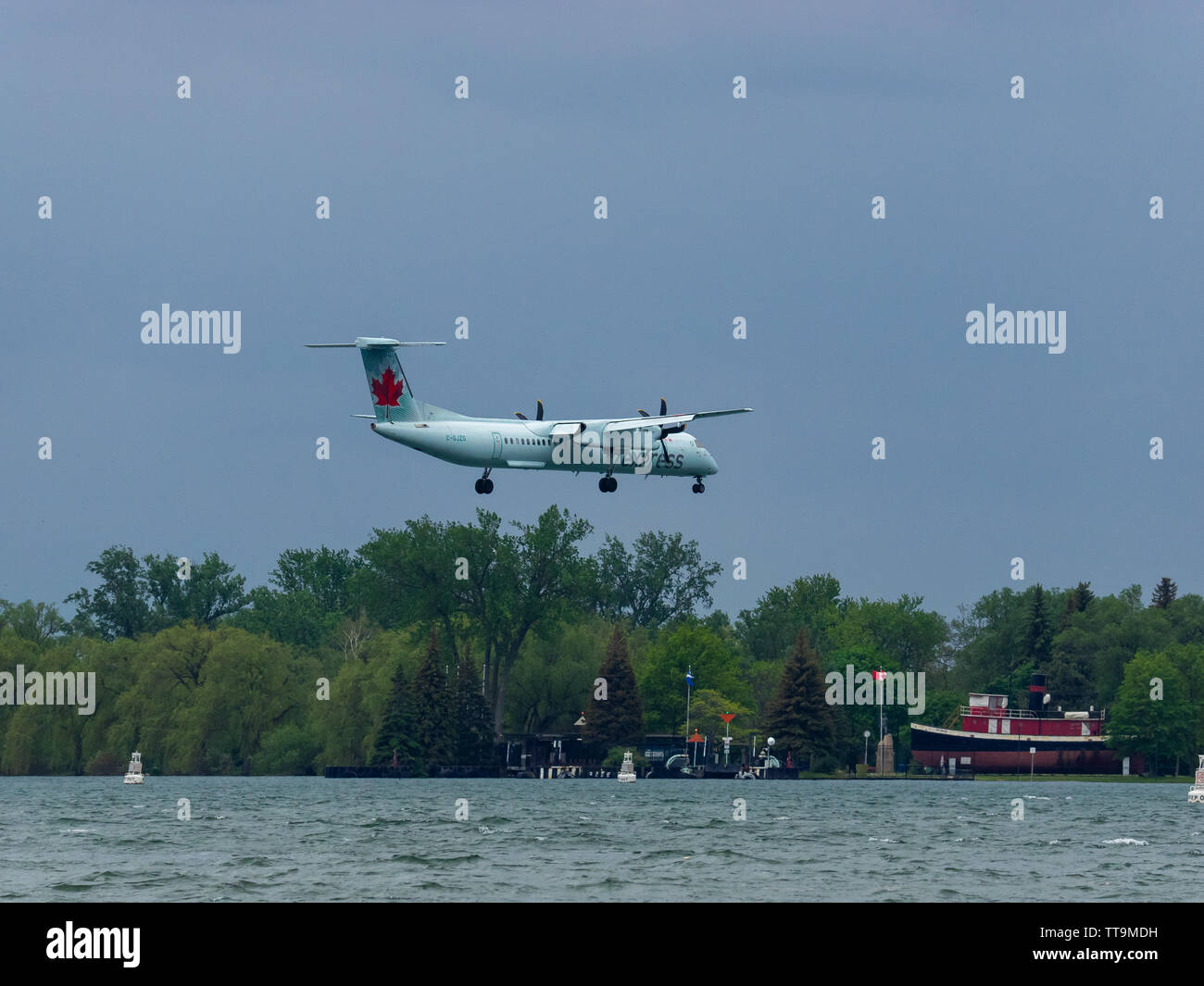 Air Canada Express De Havilland Canada DHC-8-400 flying in 33km/h or 20.5mph wind, past Centre Island on approach for landing on the island airport. Stock Photo