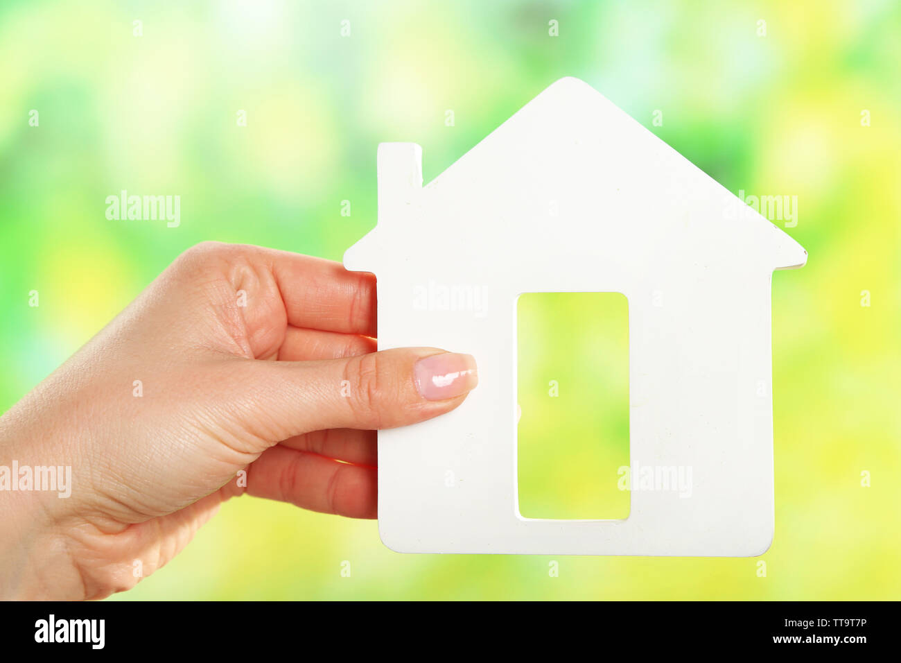 Female hand holding model of house on bright background Stock Photo - Alamy