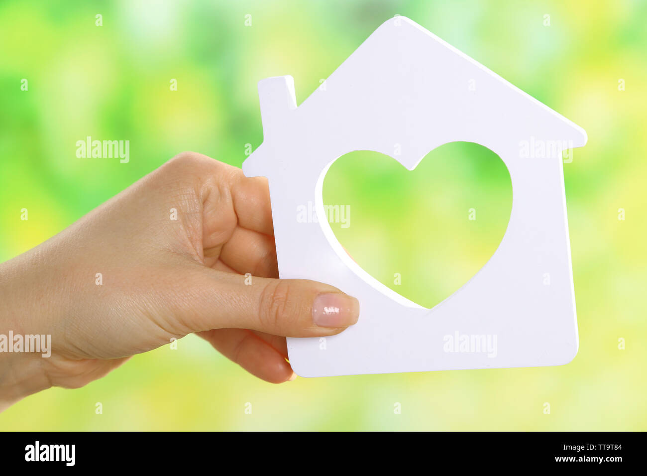 Female hand holding model of house on bright background Stock Photo - Alamy