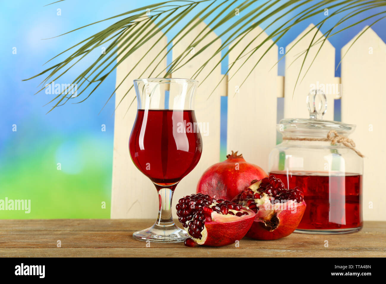 Pomegranate and glass of juice on wooden table and wight fence background Stock Photo