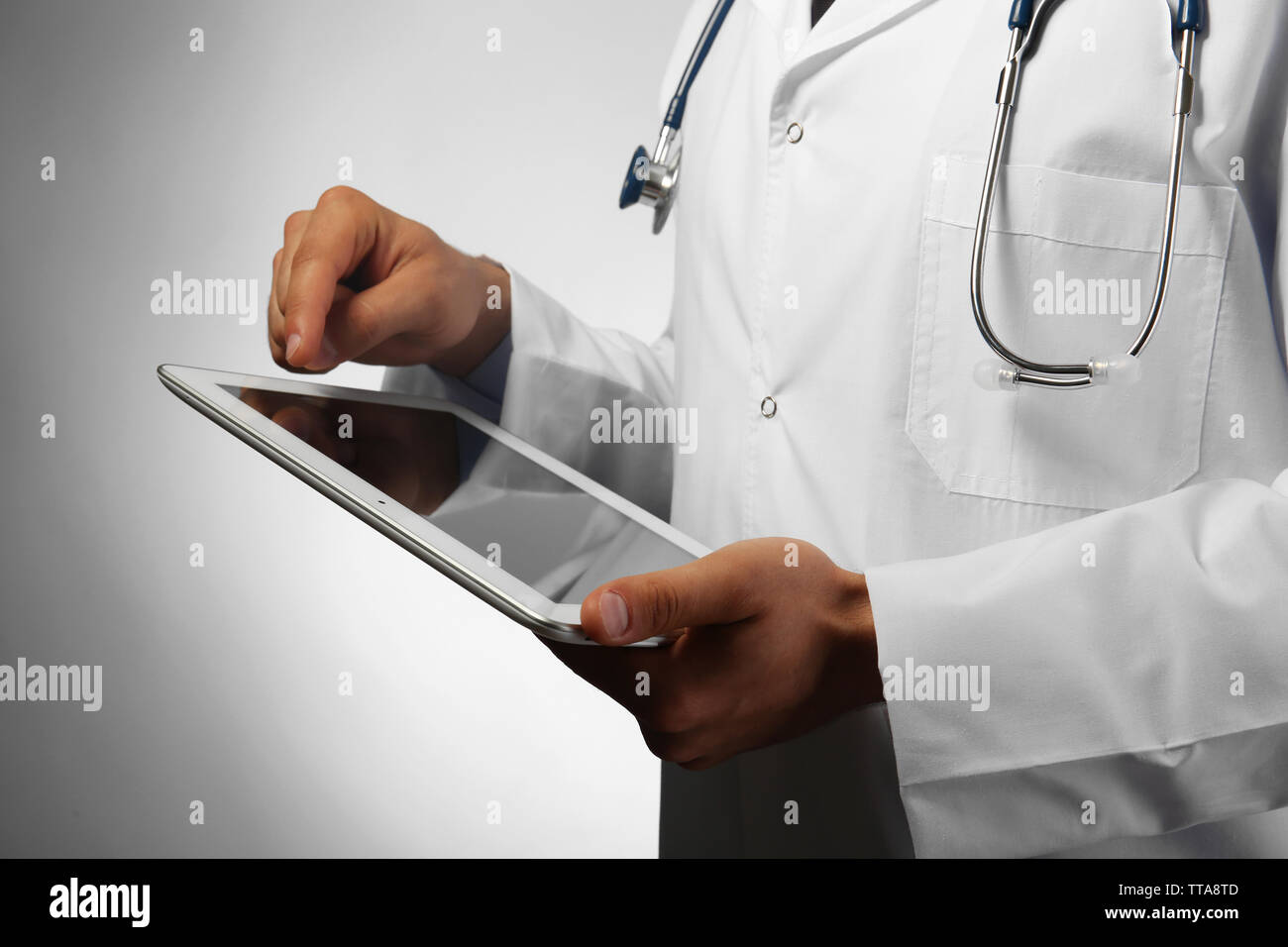 Male doctor with tablet on gray background Stock Photo - Alamy
