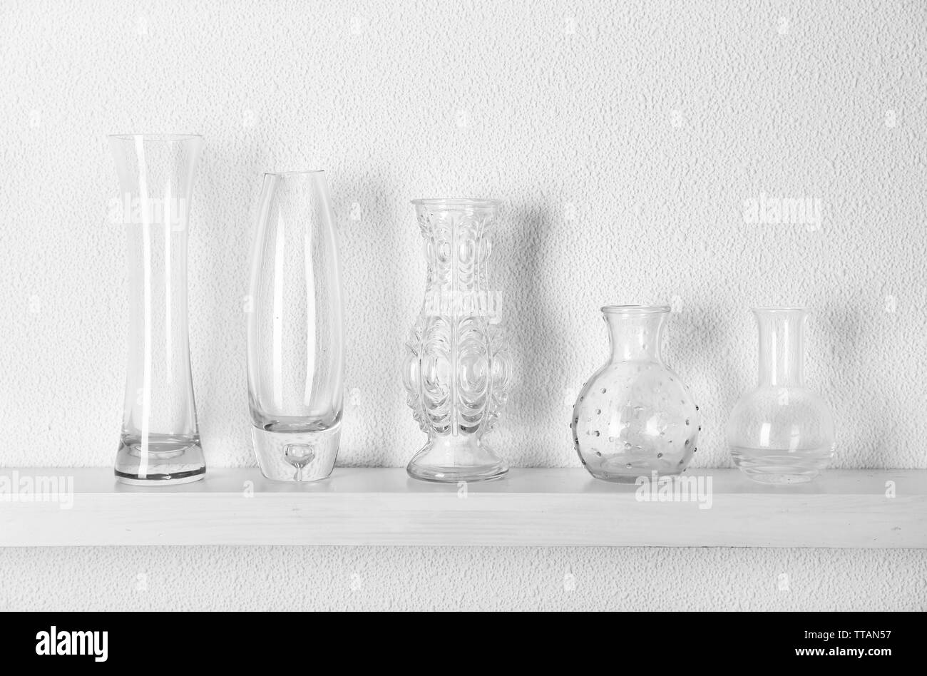 Decorative glass vases on wooden shelf on white wallpaper background