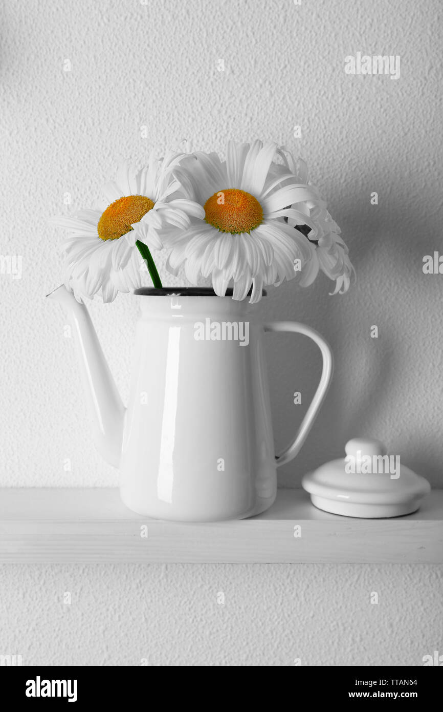 Decorative teapot with flowers on wooden shelf on white wallpaper